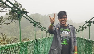 UT student Feliciano poses with hook'em horns hand sign in front of a bridge in Costa Rica
