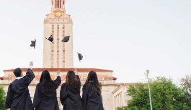 four UT grads throw up their caps in front of the tower
