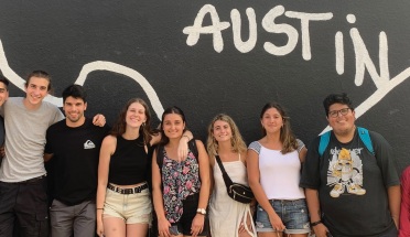 Group of students smiling in front of black mural with white outline of Texas