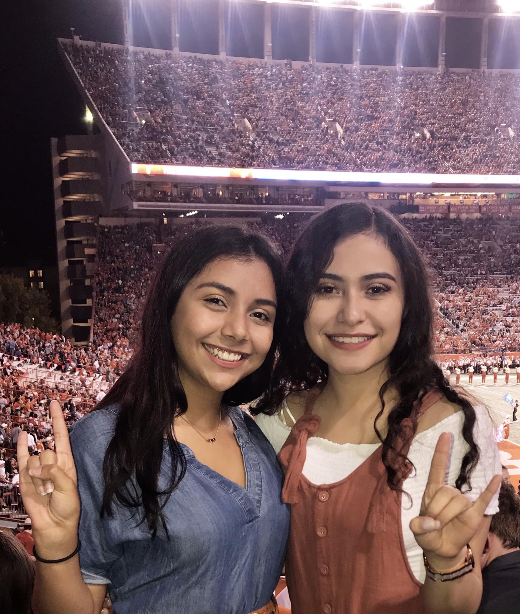 two women put up hand signs and smile in crowded stadium