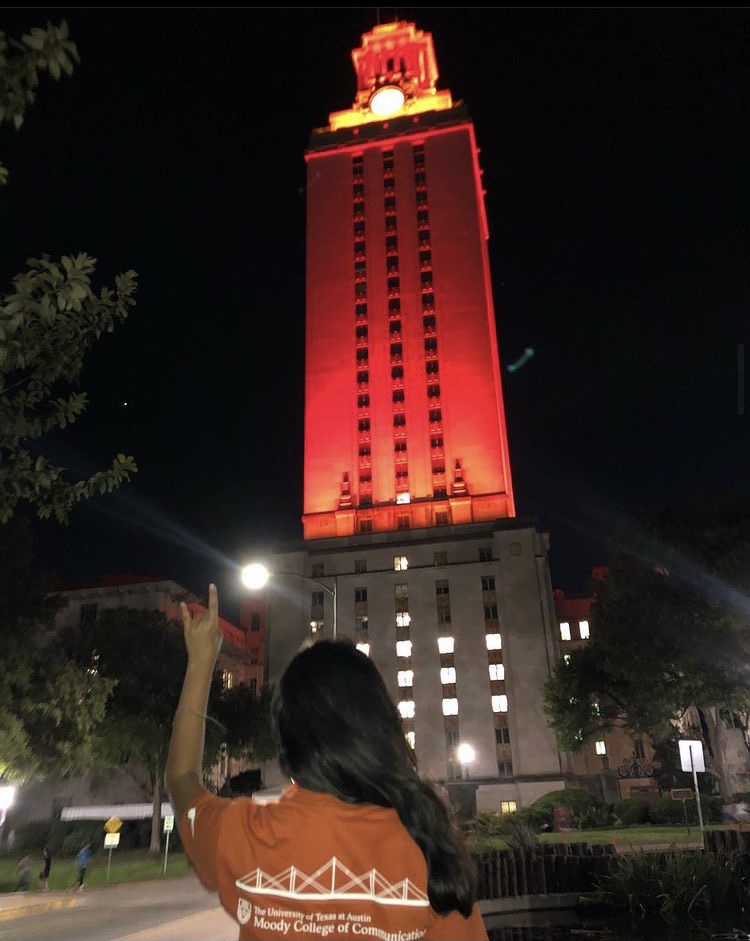 back of woman wearing orange shirt throwing up hand sign near orange-lit tower