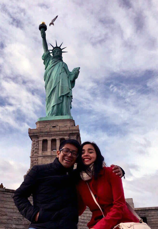 eduardo and paulina pose in front of the statue of liberty