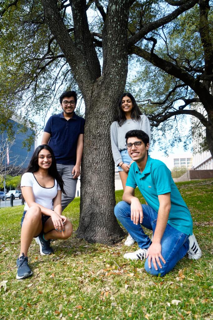 Bhalla kneels in front of a tree on campus, smiling with friends.