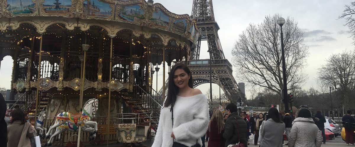 Mariana Tejada next to a carousel in Paris with the Eiffel Tower behind her.