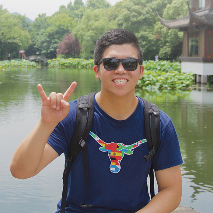 UT Student giving hook em sign in front of Asian lake