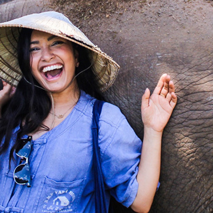 Female smiles while leaning on baby elephant in Thailand.