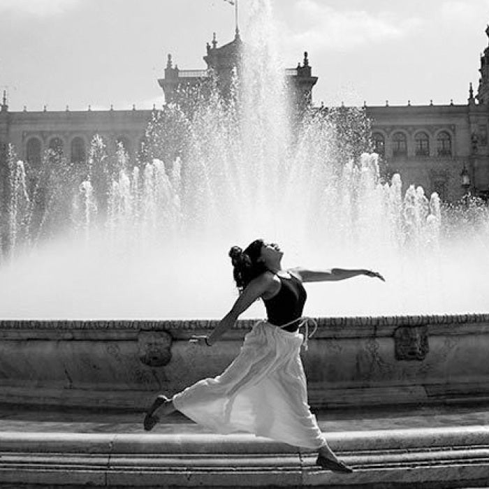A woman gracefully leaps in front of a fountain in Seville, Spain.