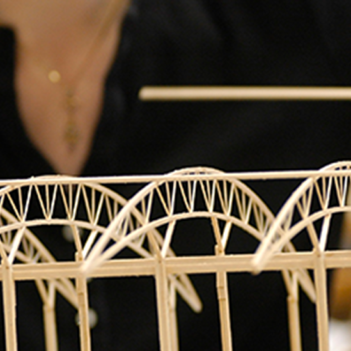 close up of person building small model of bridge with many arches with wood