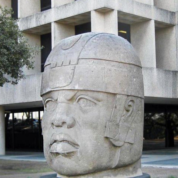 large stone bust in front of grey building near trees