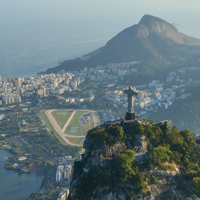 statue on mountain overlooking city near mountains and body of water during daytime