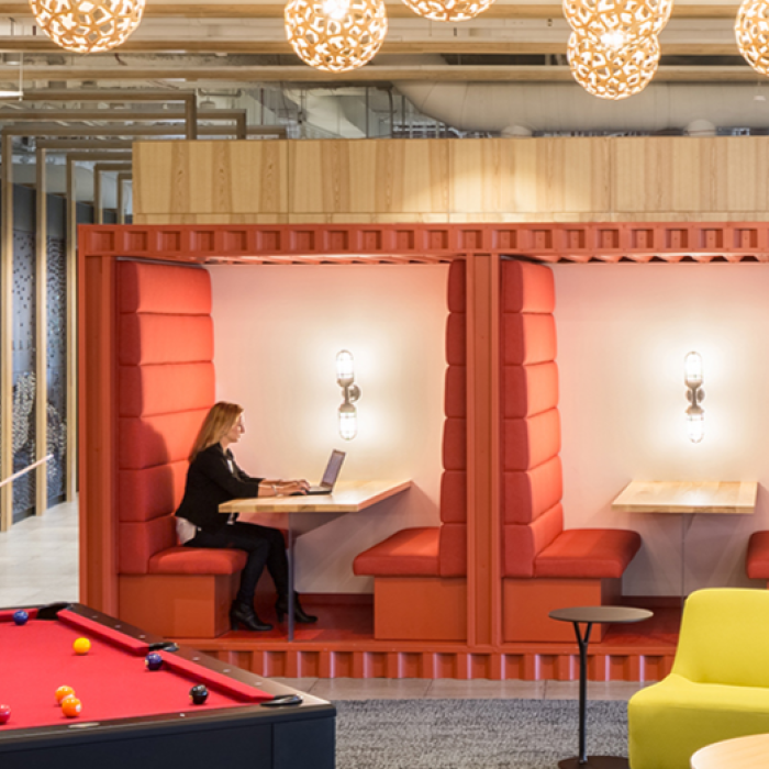 people play on pool table near people working in booths and on sofa in office workspace