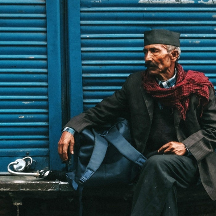 old man sitting in front of shutters with backpack 