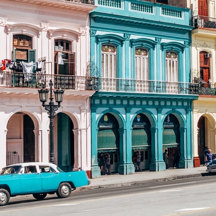 two vintage cars parked outside row of colorful buildings 