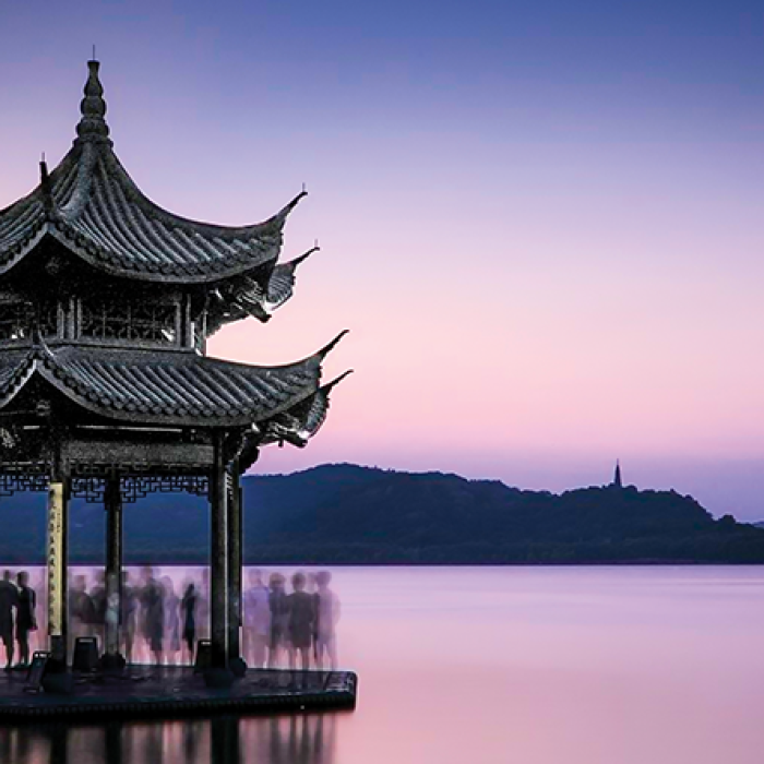 Chinese shrine on water at sunset with faded outlines of tourists visiting