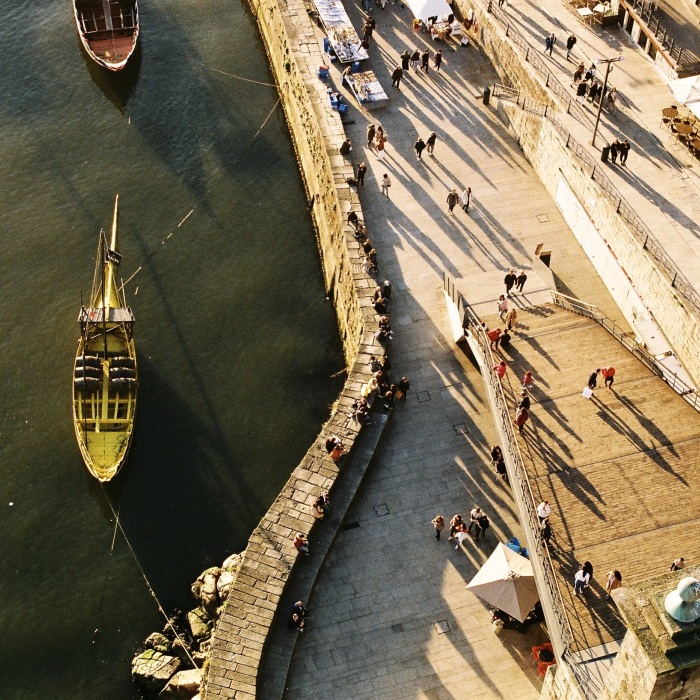 Arial view of stone boardwalk with yellow tour boat in the water and people walking, sitting, and along boardwalk and large staircase