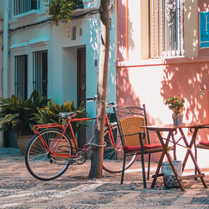 outdoor chairs and tables near colourful buildings and bicycle in shade during daytime