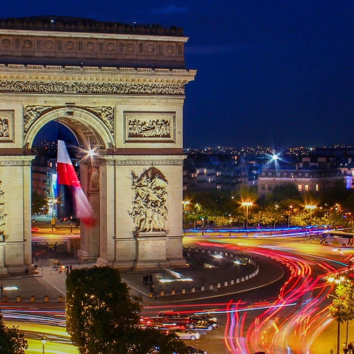 large arch near busy roadways with french flag during nighttime