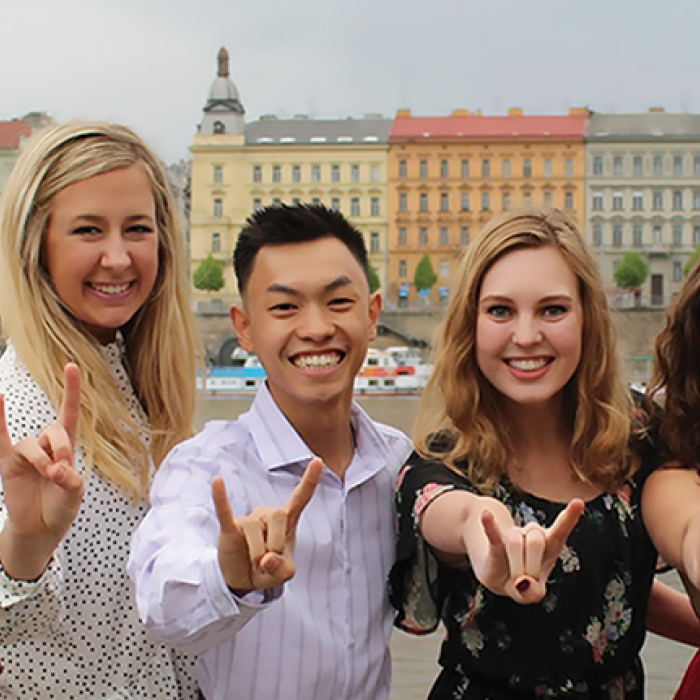 seven students doing the hook 'em sign in front of scenery