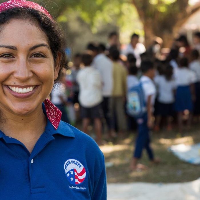 a woman peace corps volunteer smiles, wearing a peace corps shirt 