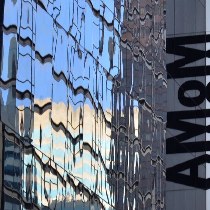 side view of glass building with letters "MoMA" written on side and reflected in windows during daytime