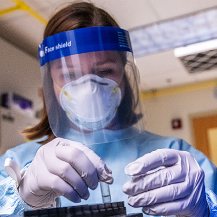 young health scientist in a mask and face shield holds a test tube