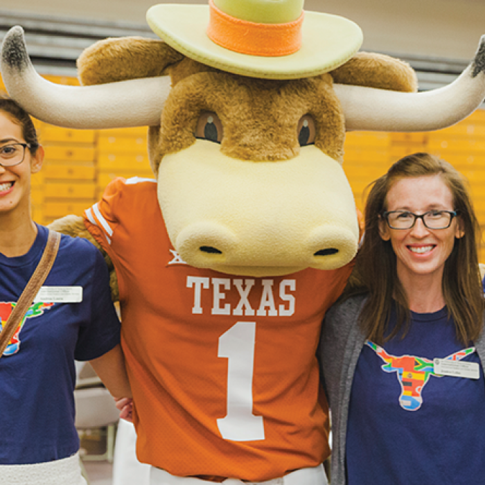 UT Students and staff wearing flag bevo shirts posing with the Hook'em mascot. 