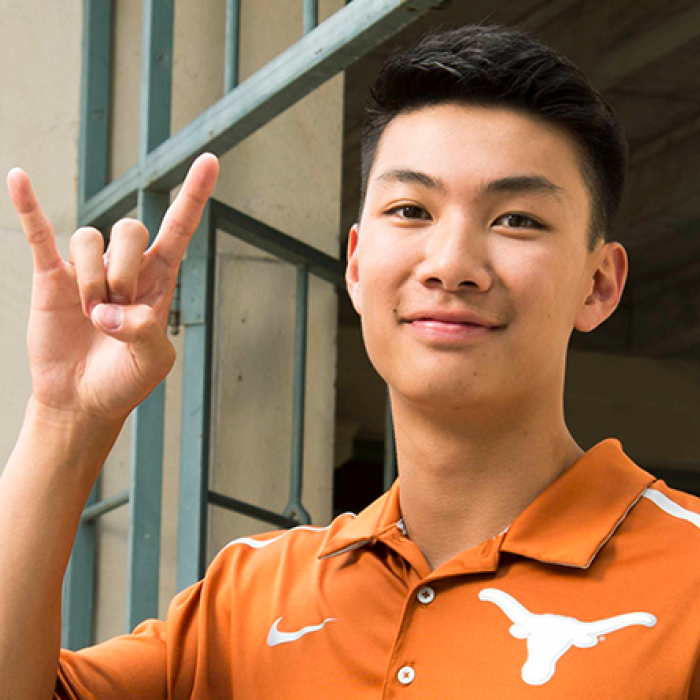 Student wearing a burnt orange shirt showing a hook'em hand sign