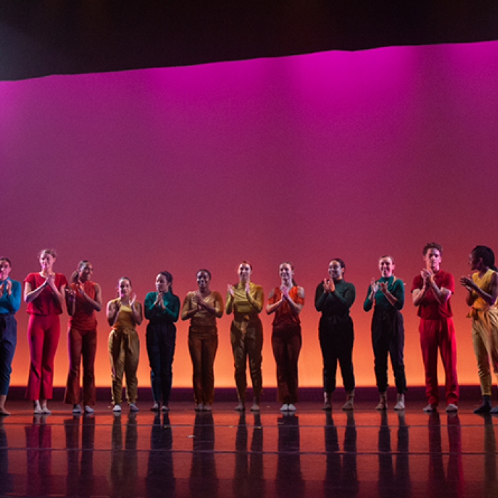 UT dance students stand on a warmly-lit stage.