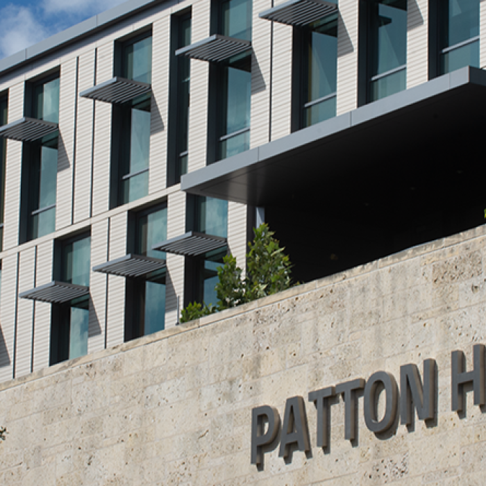 Patton Hall's large windows, limestone sign and surrounding bushes on a blue day.