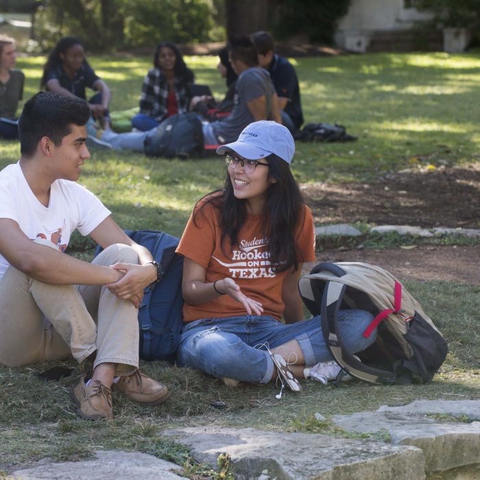 students sitting outside and talking on UT campus with other students talking in the background