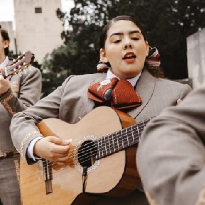 Mariachi female and male band members performing outdoors with gray suits with beige and white detailing and burnt orange ties 