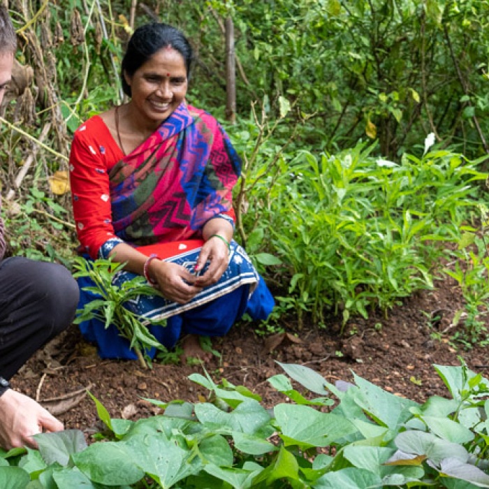 Peace corps volunteer smiles while looking at crop growth in nepal with local women wearing traditional clothing