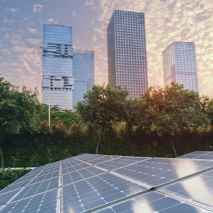 Solar panels backdropped by a city skyline and a beautiful sky