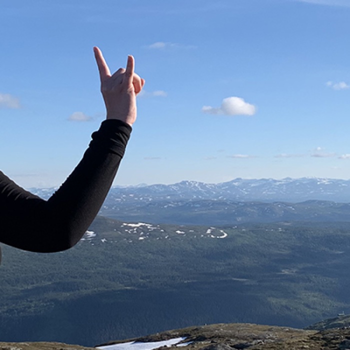 Female student throws the Hook 'Em sign at the top of the Swedish mountains