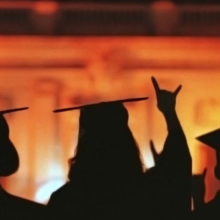 silhouettes of students in graduation caps and gowns on orange and yellow background 