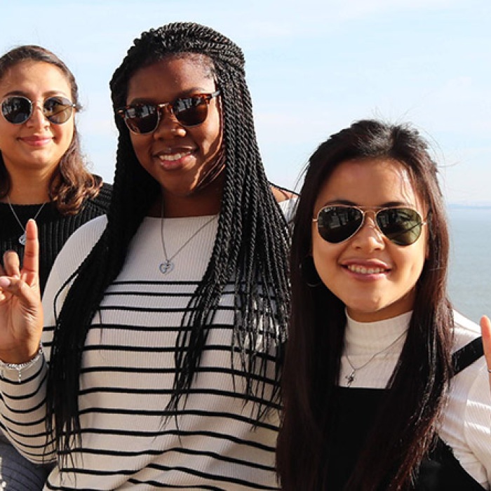 A group of UT exchange female students display the hookem sign overlooking the ocean in a foreign country.
