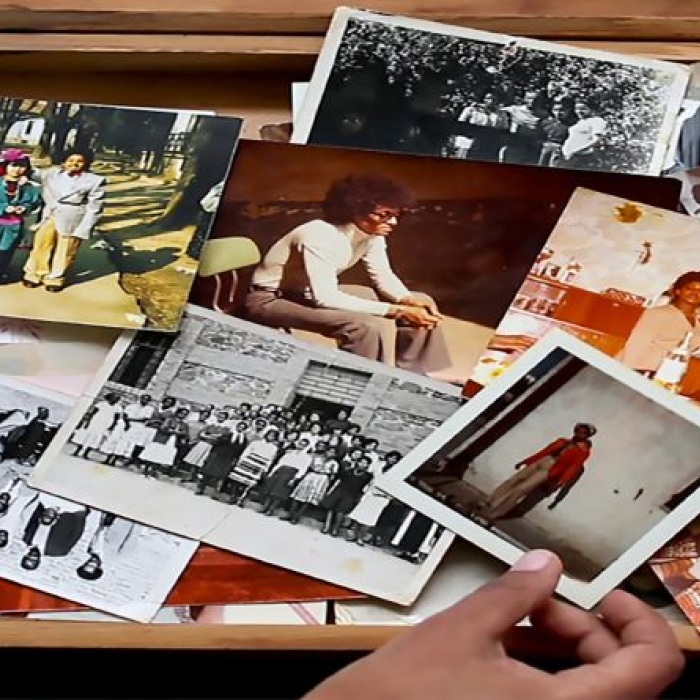 opened wooden suitcase with variety of family photographs in color and black and white with a person's hand holding one polaroid 