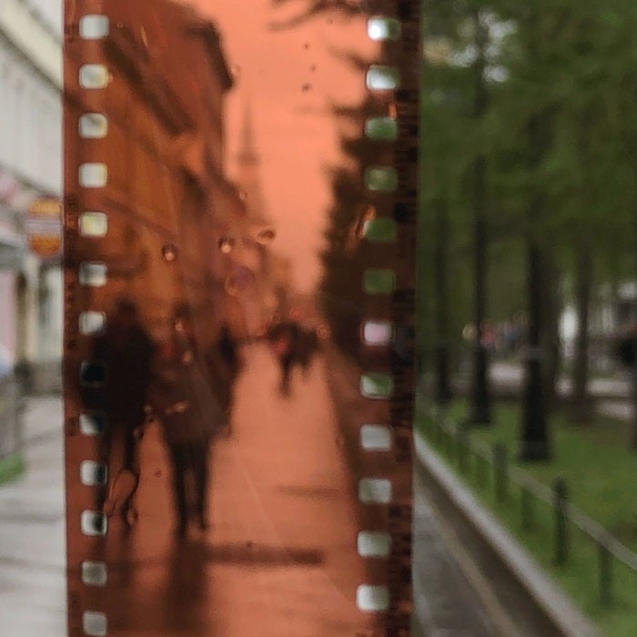 brown film held up in front of a sidewalk with trees on the right side and buildings on the left