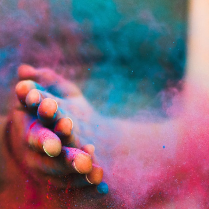 A woman's hands are surrounded by a cloud of colorful powders