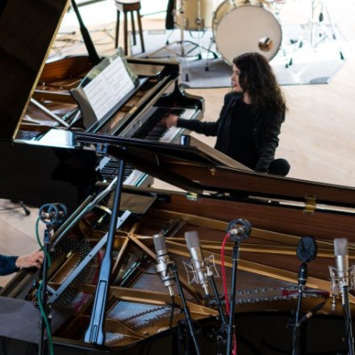 Four musicians play instruments around a grand piano