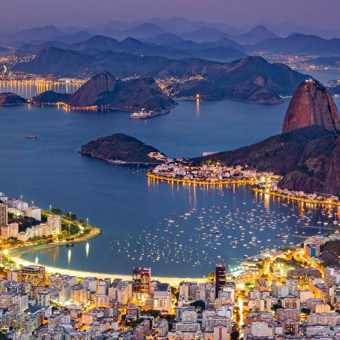 Spectacular aerial view over Rio de Janeiro as viewed from Corcovado during the blue hour of sunset. The famous Sugar Loaf mountain sticks out of Guanabara Bay.
