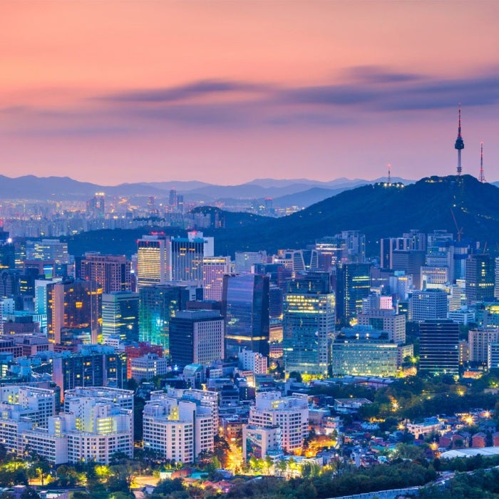 Cityscape image of colorfully lit Seoul downtown with the mountains in the background during and orange and purple summer sunrise.
