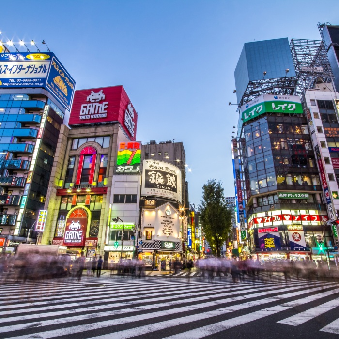 Street view of Shinjuku, Japan, illuminated with brightly colored lights and signs at night and busy with acitivity.