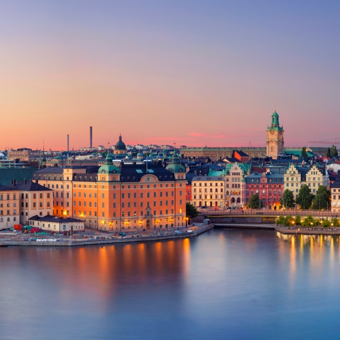 Panoramic image of Stockholm, Sweden during a beautiful pink, blue and soft yellow sunset across the still waters with reflections of the city lights.