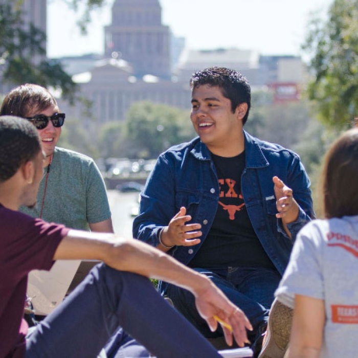 Students engaging in friendly discussion on the UT campus southlawn with Texas State Capitol in the background 