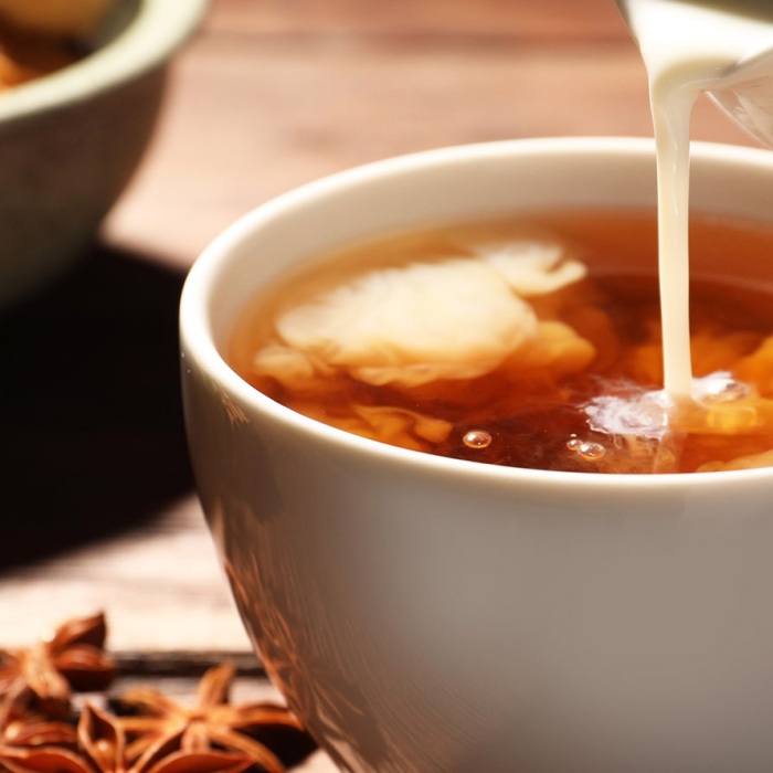 Herbs and pastries are displayed on a table as warm milk is poured into star anise tea.