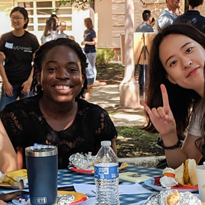 group of female international students smiling and sitting around a table together outside on UT campus
