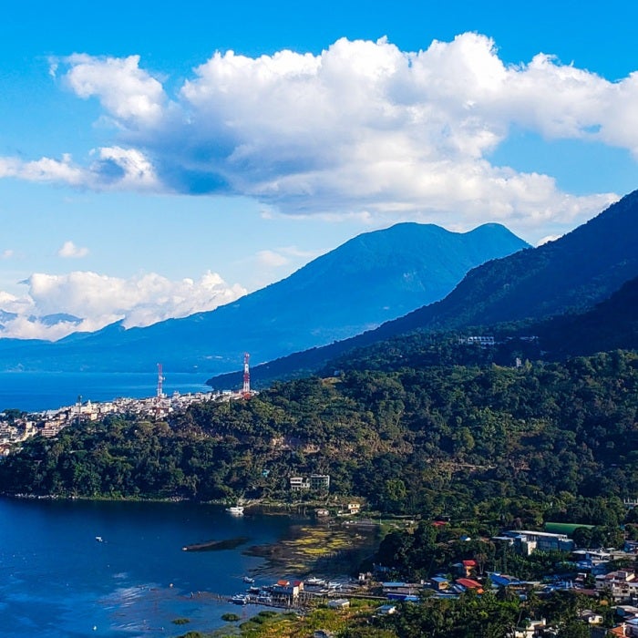 Mountains  line the shoreline of the massive Lake Atitlán as seen from San Juan La Laguna, Guatemala on a beautiful blue sky and puffy cloud day.