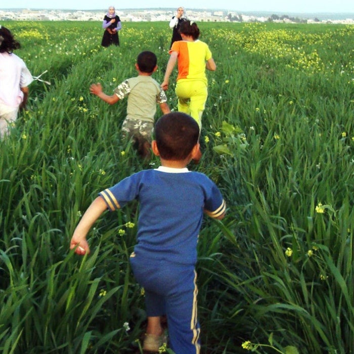 Children run thru a green field toward a Peace Corps Volunteer in the distance