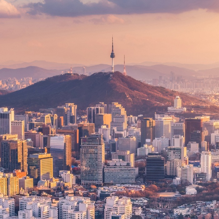 An expansive view of the city of Seoul, South Korea with the second highest point in view, marked by the N Seoul Tower during a beautiful pale pink and orange sunrise.